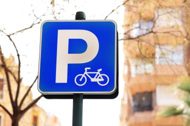 Mavi bisiklet park levhası, Avrupa şehir caddesindeki binanın arka planında bisiklet park alanlarını gösteriyor. P harfi ile işaretlenmiş bisiklet parkı. Trafik kuralları