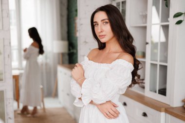 Kadınlar Günü. 20-25 yaşlarında, uzun kıvırcık saçlı, çapraz elli romantik ve çekici bir genç kadın, arka plandaki modern moda ev mutfağına bakıyor.