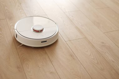 Beyaz kablosuz otonom robot elektrikli süpürgenin ahşap zemindeki en üst görüntüsü. Akıllı temizlik teknolojisi. Otomatik itişli temizlik robotu. Yer temizleme sistemi. Ev kumandası aygıtları