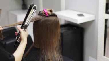 Tanımlanamayan profesyonel kuaför. Saç düzleştirici ve tarak ile kadın saçı ütülüyor. Güzellik salonunda şık bir saç stili yapıyor. Keratin, laminasyon, saç bakımı, kuaför salonu ve kuaförlük.