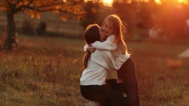 Aile günü, anneler günü. Mutlu gülümseyen genç anne ve sevimli kız çocuğu gün batımında sarılıyor, öpüşüyor ve birlikte vakit geçiriyorlar. Idyllic ailesi sonbahar tatilinde dışarıda eğleniyor.