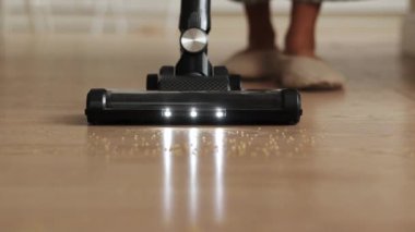 Oda hizmetleri. Tanımlanamayan kadın kablosuz elektrik süpürgesi kullanıyor mutfak çöplerini aydınlatmak için, lamine zeminden gelen gevşek inlemeler. Modern ev aletleri.