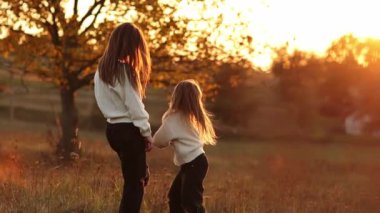 Aile günü, anneler günü. Mutlu bir anne ve güzel bir kızın el ele tutuşup sonbaharda gün batımında yürürken el ele tutuşması. Idyllic ailesi sonbahar tatilinde dışarıda eğleniyor.