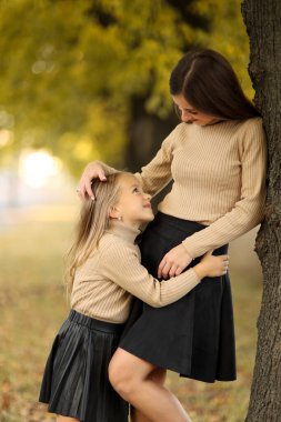 Aile günü. Genç anne ve küçük kızı sonbahar parkında eğleniyor ve dinleniyor. Sevimli kız çocuğu sıkıca sarılıyor ve annesini öpüyor. Çocuğa annelik ve sevgi. Anneler Günü.