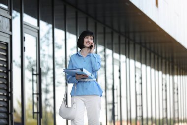 Günümüz iş kadını ya da CEO 'sunun, modern ofis binasının caddelerinde yürürken, iş ortağıyla doküman dosyalarını tuttuğu ve telefonda konuştuğu başarılı bir özgüven. İş konsepti.