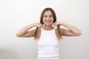 Doğal güzellik portresi, uzun saçlı, günlük kıyafetler giyen, beyaz bluz ve mavi şort giyen, beyaz arka planda izole edilmiş kameraya bakan pozitif bir genç kadın. Sağlıklı yaşam tarzı kavramı