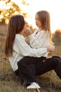 Aile günü, anneler günü. Mutlu gülümseyen genç anne ve sevimli kız çocuğu gün batımında sarılıyor, öpüşüyor ve birlikte vakit geçiriyorlar. Idyllic ailesi sonbahar tatilinde dışarıda eğleniyor.