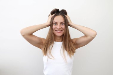 Mutlu, rahat, uzun düz saçlı, el ele tutuşan, dişleri sırıtan, kameraya bakan, arka planda izole beyaz bir üst giysisi olan mutlu, rahat, genç, doğal bir kadın..