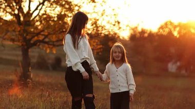 Aile günü, anneler günü. Mutlu genç anne ve sevimli kız çocuğu gün batımında yürürken el ele tutuşuyorlar. Idyllic ailesi sonbahar tatilinde dışarıda eğleniyor.