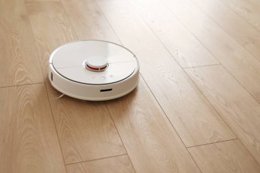 Beyaz kablosuz otonom robot elektrikli süpürgenin ahşap zemindeki en üst görüntüsü. Akıllı temizlik teknolojisi. Otomatik itişli temizlik robotu. Yer temizleme sistemi. Ev kumandası aygıtları