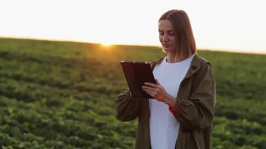 Akıllı tarım soya fasulyesi teknolojisi. Kadın çiftçi dijital tabletle çalışıyor, organik soya yeşili bitkilerle tarlalarda yürüyor. Tarım sektörü ve tarım modern konsepti. Çiftlikte tarımcı.