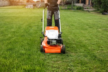 Korunaklı giysiler içindeki tanınmayan profesyonel bahçıvan arka bahçesinde modern benzin kablosuz çim biçme makinesi kullanarak yeşil çimen biçiyor. Mevsimlik peyzaj tasarımı. Bahçe işleri araçları.