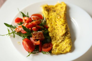 Omletli sağlıklı kahvaltı ve beyaz tabakta hardal, bal ve zeytinyağı sosuyla kaplı vişneli domates ve roka ile taze salata. Proteinli ve lifli besleyici bir yemek. Ketojenik diyet