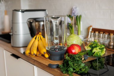 Smoothie ve yaşam tarzı diyeti için sağlıklı malzemeler. Cam blender kasesi, elma, muz, brokoli, maydanoz modern ev mutfağında masanın üstünde. Taze meyve, sebze ve sebze.