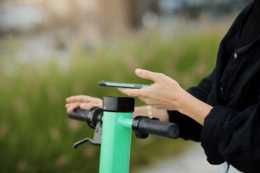 Akıllı telefonlu bir kadının kesilmiş fotoğrafı. Elektrikli scooter kiralama için QR kodunu tarıyor. Dışarıdaki limansız nakliye aracının kilidini açmak için telefondaki uygulamayı kullanan kız. Kentsel ekolojik araç. Modern teknoloji