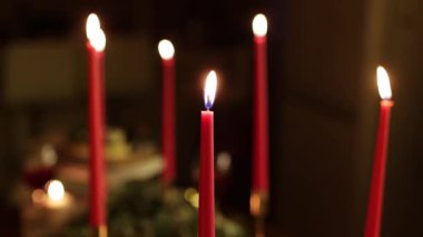 Çelenk arkaplanlı karanlık bir odada altın ışıkla yanan bir sürü uzun kırmızı mum. Noel, ev içi dekoratif ışıklandırma ekipmanlarıyla yeni yıl kurulumu