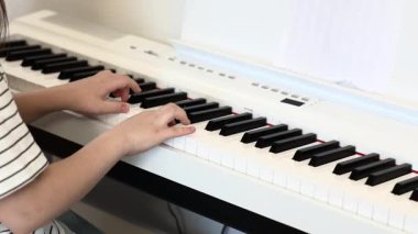 Müzik stüdyosunda, okulda siyah beyaz klavyeyle dijital piyano çalan küçük kız müzisyenin ellerini kapatın. Evde sentezleyiciyle müzik öğrenen tanınmayan bir çocuk. Hobi