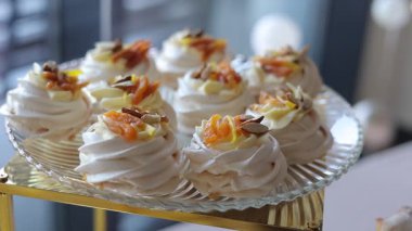 Krem şanti ve pudra şekerle doldurulmuş, böğürtlen, meyve ve fındıkla süslenmiş mini kremalı pavlova tatlısı. Cam tabakta ve altın tezgahta sunulan şenlikli tatlılar. Düğün, doğum günü kutlaması