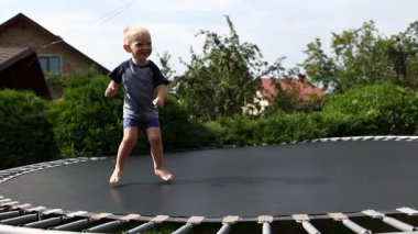 Mutlu küçük çocuk eğleniyor ve trambolinde zıplıyor, evin arka bahçesinde güneşli bir yaz günü, yaz tatilinde aktif bir eğlence. Mutlu çocukluk kavramı. Çocuk Günü.