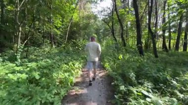 Yetişkin bir adamın yeşil orman yolunda kablosuz kulaklıklarla koştuğunu yazın müzik dinlediğini görüyorum. Aktif yaşam tarzı, sağlıklı alışkanlıklar ve motivasyon konsepti. Doğada egzersiz..