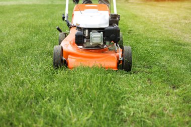 Bahçıvanlık aletleri. Turuncu elektrikli çim biçme makinesinin geniş açılı görüntüsü, tekerlekler, arka bahçedeki parlak yemyeşil çimlerin üzerinde motor. Döner çim biçme makinesi çimleri kesti. Profesyonel bahçe bakımı hizmeti.