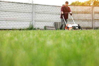 Sıradan giysiler içinde bir adam evinin arka bahçesinde çim biçme makinesiyle çim biçiyor. Baharın bulutlu olduğu bir günde koca bahçeyle ilgilenir. Modern benzin bahçesi ekipmanları. Peyzaj işi.