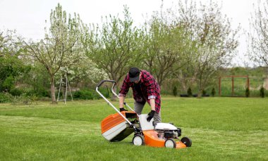 Günlük kıyafetli bir adam, kendi arka bahçesinde çim biçtikten sonra çim biçme makinesi kesilmiş bir çanta alır. Kocası bahçeyle ilgilenir. Modern benzin bahçesi ekipmanları. Evde peyzaj işi.