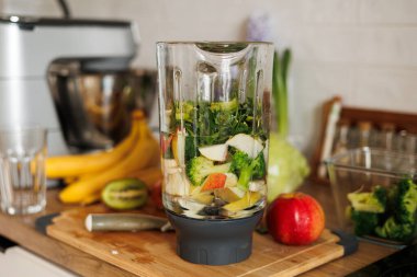 Elma, muz ve brokoli dilimli cam blender kasesi, maydanoz ve su ev mutfağının ahşap masasında. Sağlıklı detoks smoothie ve yaşam tarzı diyeti. Meyve parçaları..