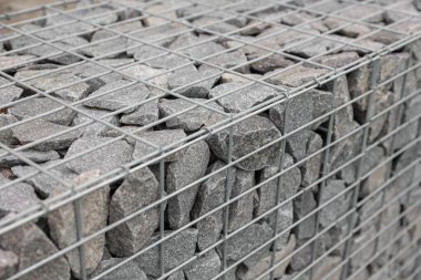 Çelik ağ ve yeşil çimenlikte taş çitler. Gabion 'u sıkıca paketlenmiş, değişik boyutlarda ve dokularda taşlarla kapatın. Doğal malzemelerin ve endüstriyel tasarımın kombinasyonu.