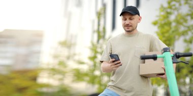 Telefon kullanan genç teslimatçının portresi açık alanda park halindeki scooter 'ın yanında karton kutular tutuyor. Sürdürülebilirlik kavramı, dağıtım ve çevre dostu modern yaşam tarzı