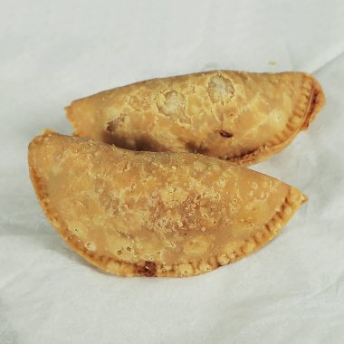 Two traditional empanadas on a white paper background. Toned.