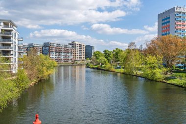 Berlin, Almanya - 28 Nisan 2022: Spree Iburger Ufer Nehri kıyıları ve Am Spreebord, burada Roentgenbruecke Köprüsü 'nden görülen modern yerleşim evleri ile Landwehr Kanalı (Spreekreuz) ile bir araya gelir.