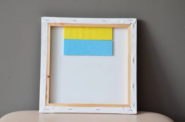 Flag of Ukraine in an art frame under an art canvas.  Awooden frame with a blue and white background.