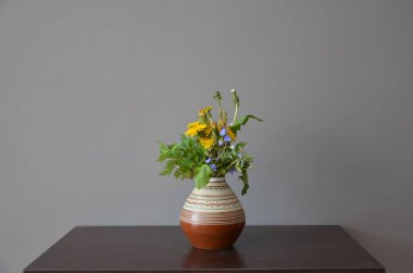 Beyaz duvara karşı tahta masada çiçekli vazo.