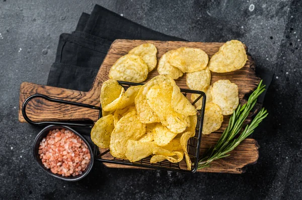 Sepette deniz tuzu ve biberiyeli patates cipsi. Karanlık arka plan. Üst görünüm.