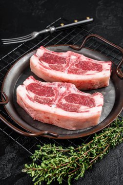 Raw fresh lamb loin chops with herbs and spices in steel tray. Black background. Top view.