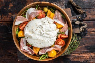 İtalyan domatesleri ve roka, jambon ve zeytinli burrata peynirli salata. Ahşap arka plan. Üst görünüm.