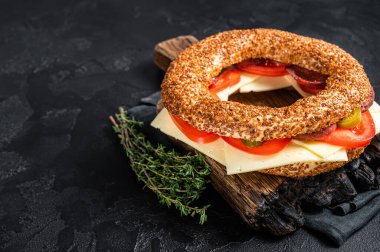 Simit bagel sandwich with lettuce, tomato, yellow cheese and ham. Black background. Top view. Copy space.