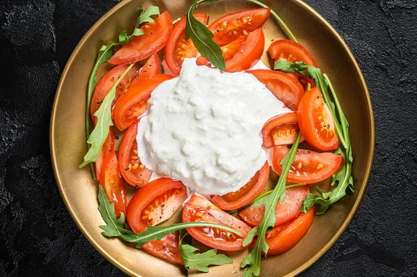 İtalyan salata caprese peynirli stracciatella, domates ve roka. Siyah arka plan. Üst görünüm.