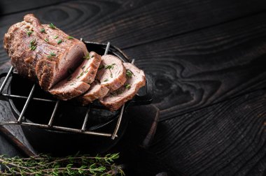Roast beef on a grill, tenderloin sliced meat with herbs. Black Wooden background. Top view. Copy space.