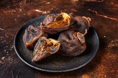Dried persimmon fruit on a plate. Dark background. Top view.