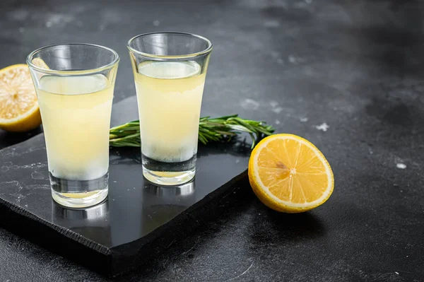 Traditional italian lemon alcohol drink liqueur limoncello with lemon and rosemary. Black background. Top view. Copy space.