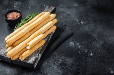 Italian grissini or salted bread sticks on wooden board. Black bakground. Top view. Copy space.