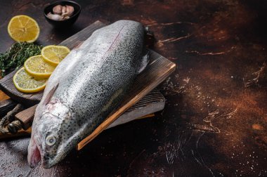Whole trout, raw fish on a wooden board with thyme and lemon. Dark background. Top view. Free space for your text.
