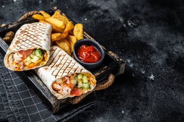 Durum doner kebab or Shawarma with meat, vegetable salad and french fries. Black background. Top view. Copy space.