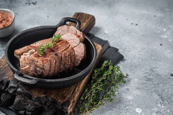 Roast Beef tenderloin, roasted meat in skillet with thyme. Gray background. Top view. Copy space.
