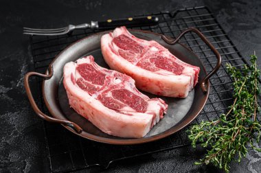 Raw fresh lamb loin chops with herbs and spices in steel tray. Black background. Top view.