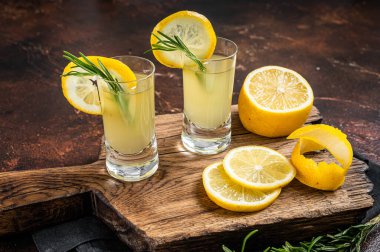 Italian limoncello liqueur and fresh lemons on a rustic wooden board. Dark background. Top view.