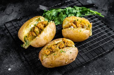 Turkish Kumpir, baked potatoes stuffed with cheese, bacon, salty cucumber, herbs and butter. Black background. Top view.