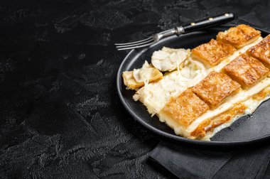 Turkish Su Boregi pie, Tabla borek or burek in plate. Black background. Top view. Copy space.